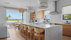 A modern kitchen with a large island, bar stools, and a view of the beach.