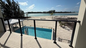 A balcony with a pool, overlooking a beach with clear skies and calm waters.