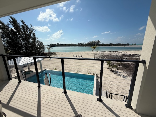 Ein Balkon mit Pool, der auf einen Strand mit blauem Himmel und ruhigem Wasser blickt.