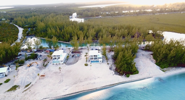 An aerial view of a coastal property with a large building, a swimming pool, and a beach area.