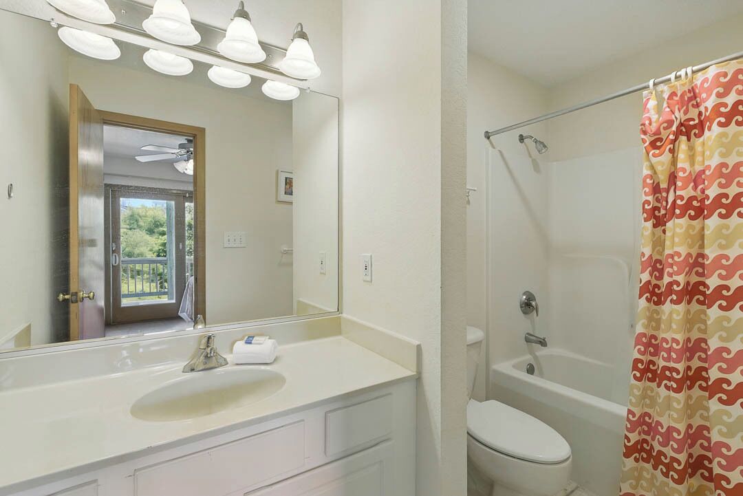 A bathroom with a white sink, a mirror, a shower curtain with a wavy pattern, and a toilet.