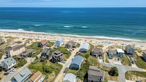 An aerial view of a coastal residential area with houses, a beach, and the ocean.