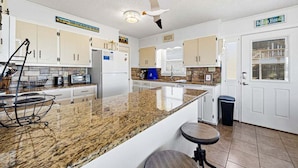 A kitchen with granite countertops, white cabinets, a ceiling fan, and a trash can.