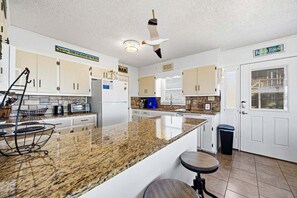 A kitchen with granite countertops, white cabinets, a ceiling fan, and a trash can.