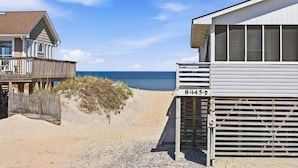 A beachside building with a number '8445-D' on the side, a wooden deck, and a view of the ocean.