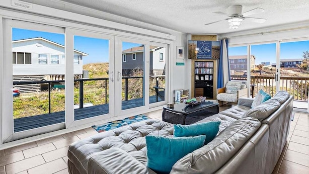 A spacious living room with a large leather sofa, a coffee table, and a bookshelf.