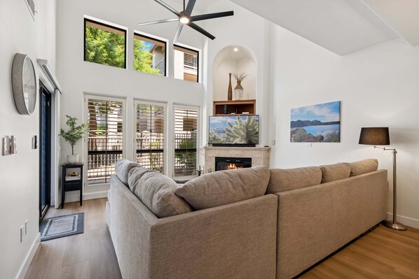 A modern living room with a sectional sofa, a fireplace, and a ceiling fan.