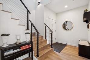 A staircase with a black railing, a white door, a round mirror, and a console table with decorative items.