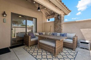 A covered patio area with wicker furniture, a stone pillar, and a glass door leading to a room.