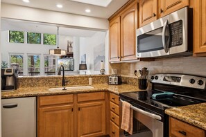 A kitchen with granite countertops, wooden cabinets, stainless steel appliances, and a view through the window.