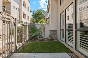 A courtyard with a metal gate, a small lawn, potted plants, a decorative wall, and a building with large windows. - Modern 3-Bed, 3-Bath Townhouse in the Heart of Scottsdale (Scottsdale)