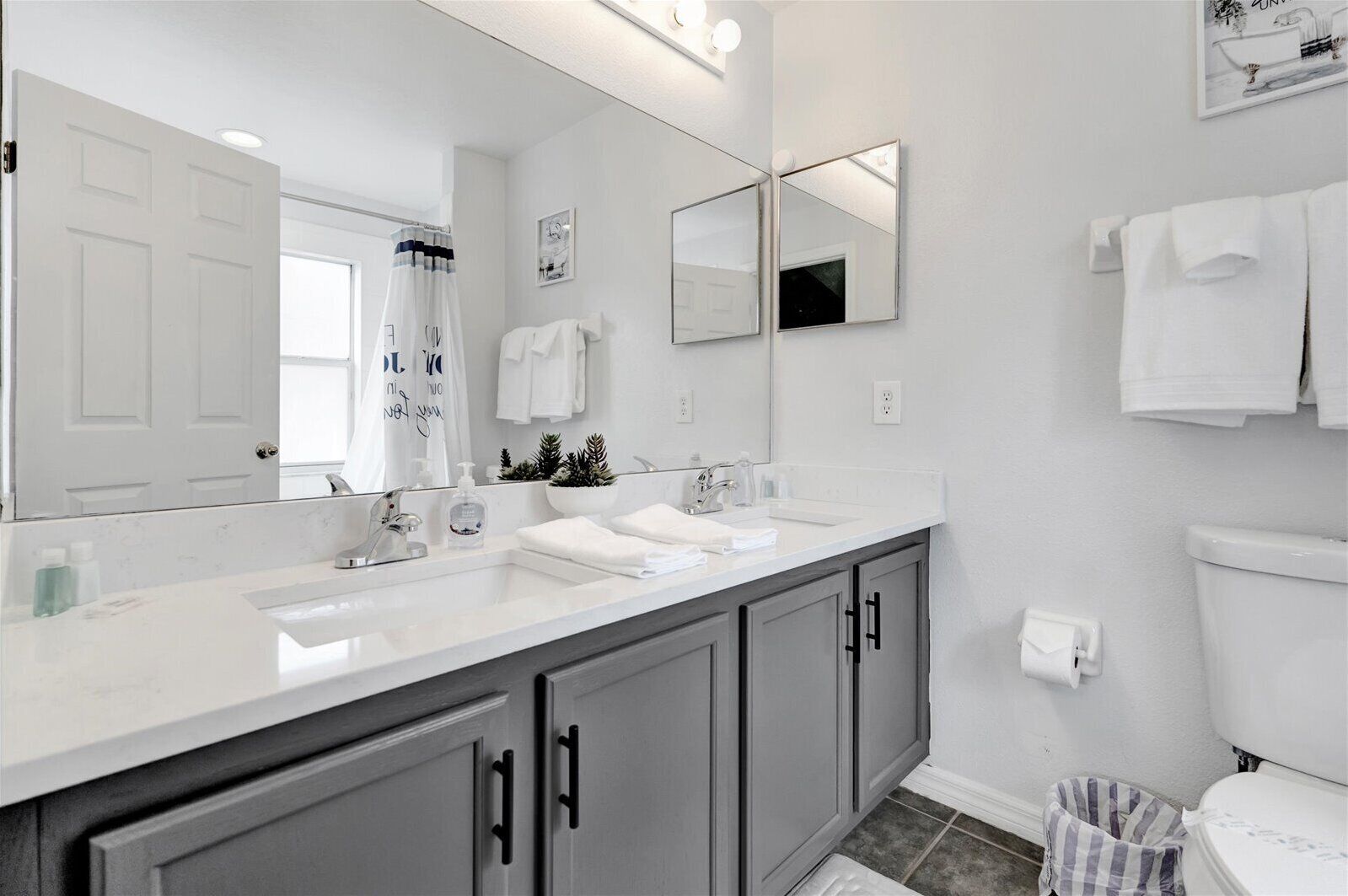 A modern bathroom with a large mirror, two sinks, and a toilet.