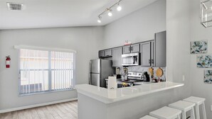 Una cocina moderna con armarios grises, encimera blanca y refrigerador de acero inoxidable.