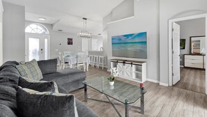 Una sala de estar moderna con un sofá gris, una mesa de centro de vidrio y un comedor con sillas blancas y una mesa.