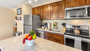A kitchen with wooden cabinets, stainless steel appliances, a marble countertop, and a fruit bowl. - Tropical stay with full kitchen (Kihei)