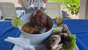 A seafood dish with a lime garnish on a white plate, set on a blue tablecloth at a beachside location with a thatched umbrella and chairs. - Hotel nuevo amanecer (Chiquimulilla)