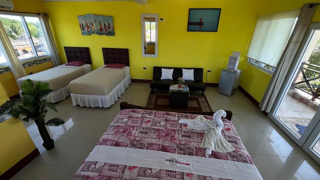 A hotel room with two beds, a sofa, a small table, and a potted plant.