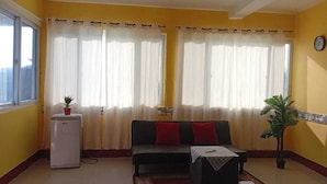 A living room with a sofa, a small table, a refrigerator, and a potted plant. - Hotel nuevo amanecer (Chiquimulilla)