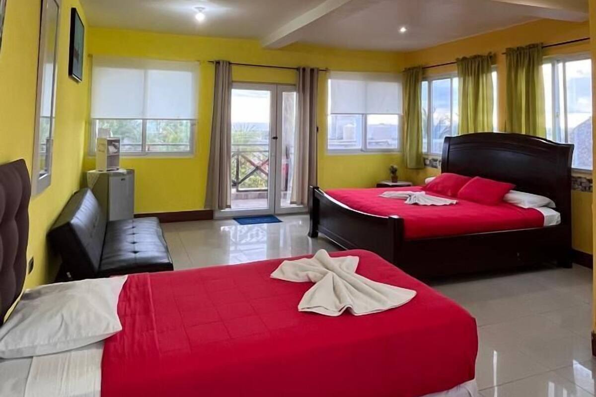 Habitación de hotel con dos camas, un sofá y una ventana con cortinas.