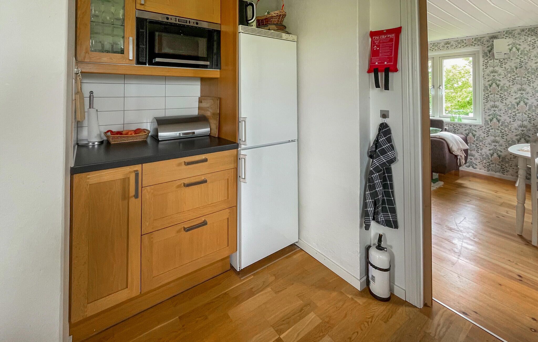 Una cocina compacta con armarios de madera, microondas, refrigerador y una manta ignífuga en la pared.