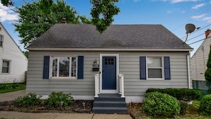 A single-story house with a dark blue front door, white shutters, and a number '135' sign above the door. - Modern Home 3 Minutes from Airport! (Cheektowaga)