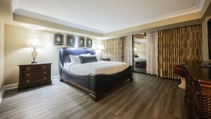 Une chambre d’hôtel avec un grand lit, une table de chevet, une lampe, une chaise et une vue sur l’extérieur par une fenêtre munie de rideaux.