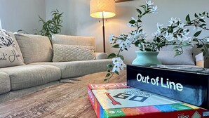 A living room with a sofa, a wooden coffee table, a lamp, and a box of Monopoly game pieces. - Gorgeous 3-bedroom 4 bed home in San Diego (San Diego)
