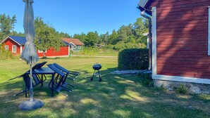 Ein Garten mit Esstisch, Stühlen, Sonnenschirm und Grill.