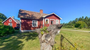 Ein rotes Holzhaus mit Ziegeldach, umgeben von einem gepflegten Rasen und einem großen Baumstumpf im Vordergrund.