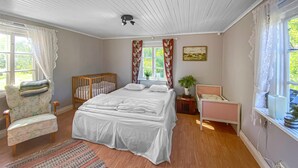 Ein Schlafzimmer mit einem großen Bett, einem Holckindbett, einem Sessel und einem Fenster mit Vorhängen.