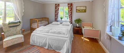 Une chambre à coucher avec un grand lit, un berceau en bois, une chaise et une fenêtre avec des rideaux.