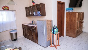 Een keuken met houten kasten, een roestvrijstalen koelkast, een tafeltje met een vaas en een afvalbak.