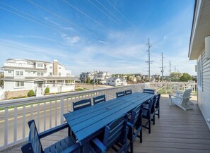 Eine Holzterrasse mit Tisch und Stühlen, mit Blick auf eine Straße mit Häusern und Stromleitungen.