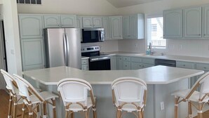 A modern kitchen with white cabinets, a central island with bar stools, and a stainless steel refrigerator.