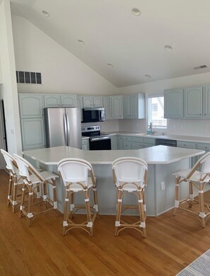 A modern kitchen with white cabinets, a central island with bar stools, and a stainless steel refrigerator.