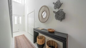 A hallway with a dark console table, wicker baskets, a woven mirror, and turtle wall art.