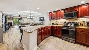 Una cocina moderna con encimeras de granito, armarios de madera, una estufa de acero inoxidable y una isla grande con taburetes de bar.