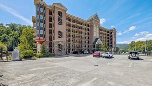 Un hotel de varios pisos con un patio central, zona de estacionamiento y montañas al fondo.