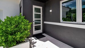 Un edificio moderno con fachada oscura, ventana de marco blanco y un arbusto verde en primer plano.
