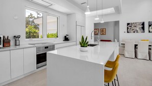 Una cocina moderna con armarios blancos, una isla central y un comedor con sillas amarillas.