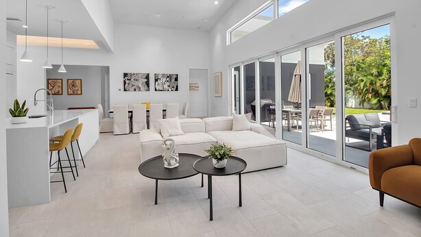 Un salón amplio con un sofá blanco, una mesa de comedor y una zona de cocina con barra.