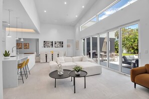 Een ruime woonkamer met een witte bank, een eettafel en een keukenbar.