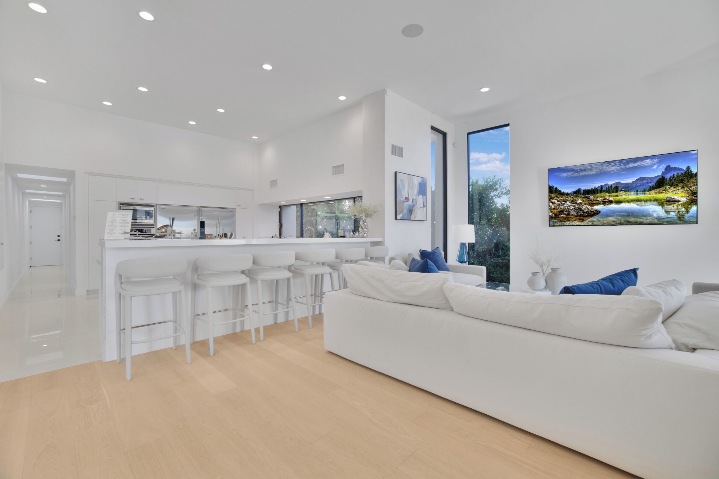 A modern, white interior with a kitchen area, a white sofa, and a large window with a scenic view.