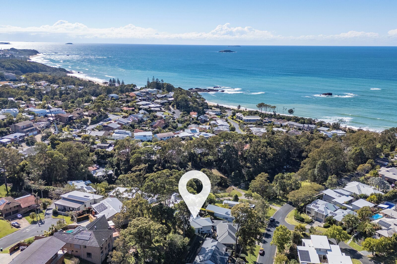 An aerial view of a coastal residential area with houses, roads, and a beach.