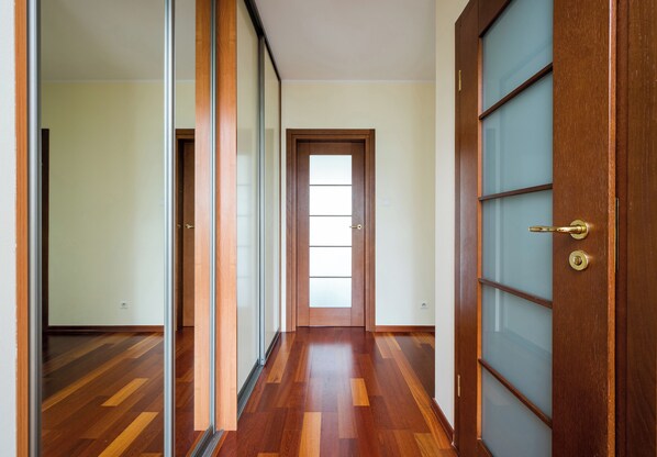 A hallway with wooden flooring, a glass door, and a wooden door with a brass handle.