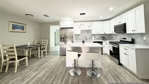 A modern kitchen with white cabinets, stainless steel appliances, and a central island with bar stools. - Home Near Clearwater Beach (Clearwater)