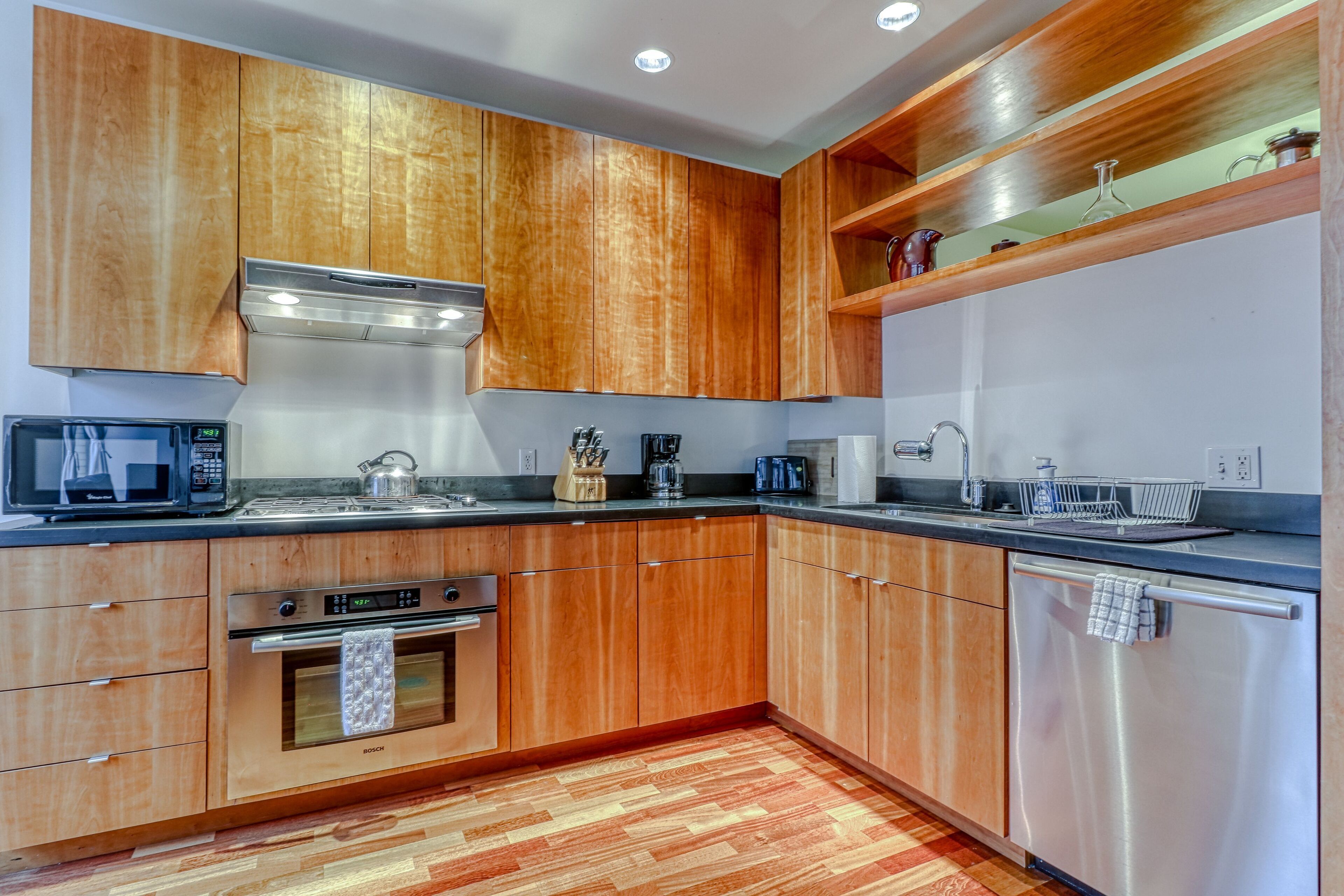 A modern kitchen with wooden cabinets, stainless steel appliances, and a wooden floor.