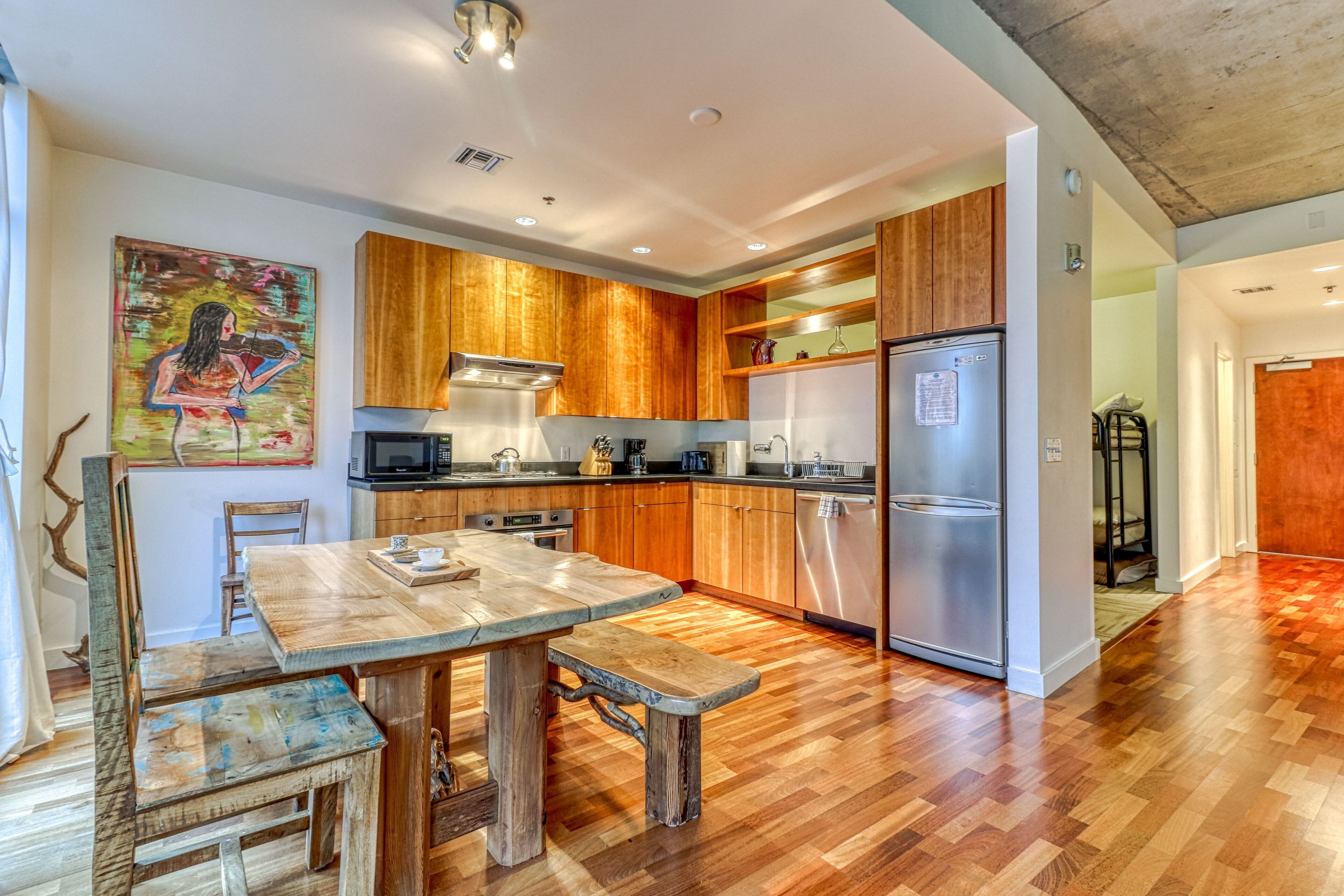 A modern kitchen with wooden cabinets, a stainless steel refrigerator, and a dining area with a wooden table and bench.