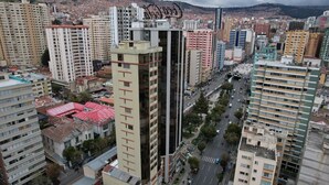 Un edificio alto con varios pisos, rodeado de otros edificios y una calle concurrida.