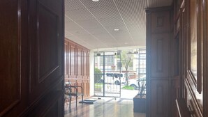 Pasillo con paneles de madera y suelo de baldosas que conduce a una puerta de cristal con celosía metálica.